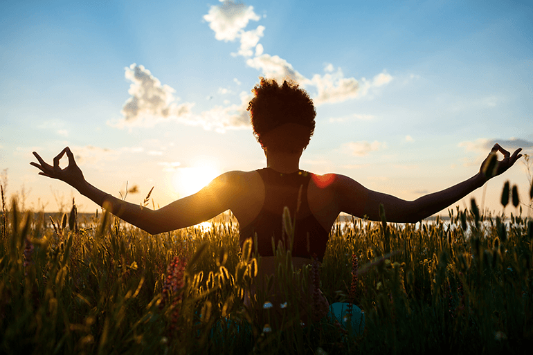 Femme pratiquant la méditation en pleine conscience dans un champ au coucher du soleil pour cultiver la paix intérieure