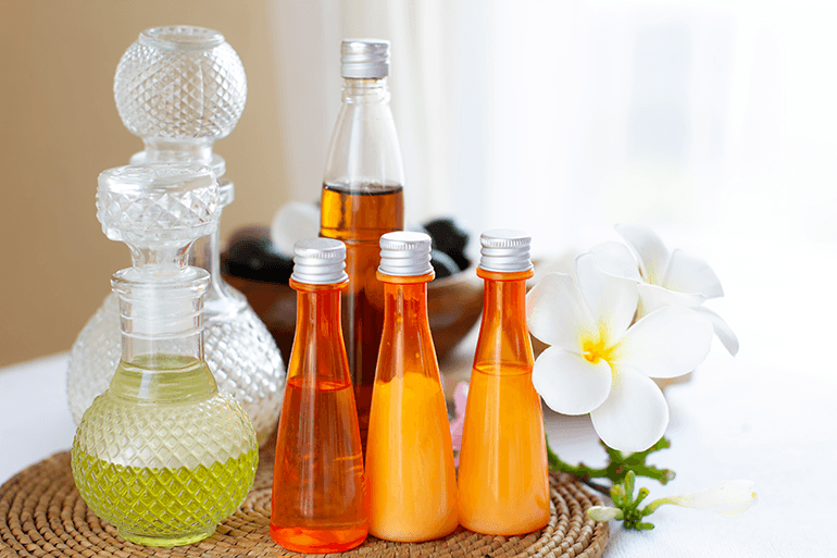 Flacons d'huiles de massage essentielles et fleurs de frangipane posés sur un support naturel pour une séance de bien-être