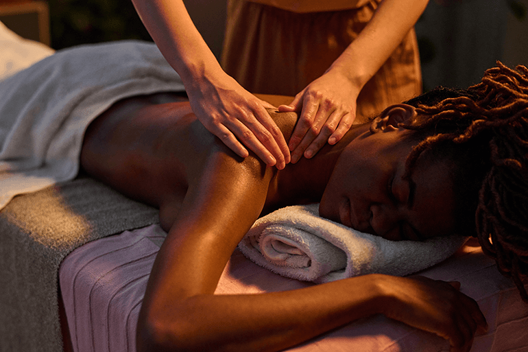 Mains d'un thérapeute massant les épaules d'une femme pour une profonde relaxation musculaire dans une ambiance tamisée